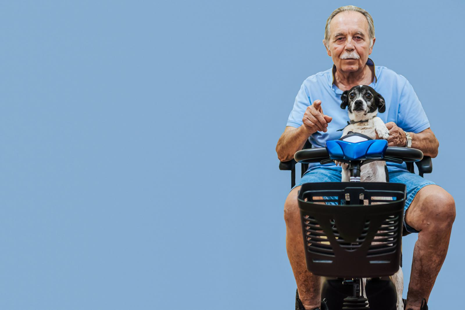 Image of an elderly man sitting on a mobility scooter with his dog in front of him.