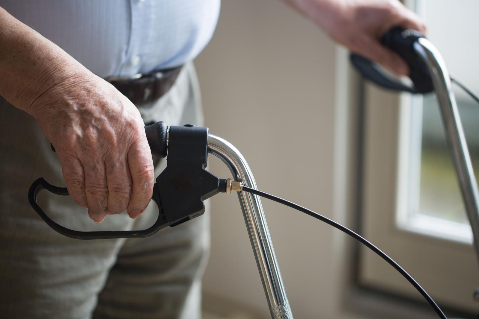 Image of a man with his hands on the handle bars of a rollator.